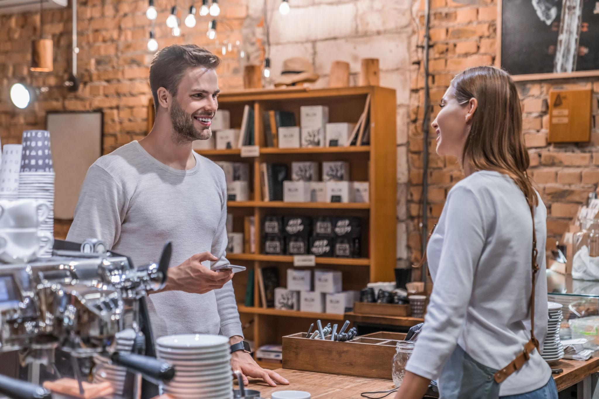 Customer holding a phone while speaking with a barista at a warm coffee shop counter